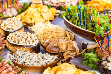 Banquet table with meat products, pistachios, olives, dried fish, chips and other snacks