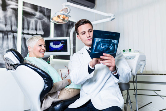 Handsome dentist looking at x-ray image of his senior woman patient. 
