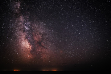 Background of bright and night-starry sky with the Milky Way upon on it and light over the water