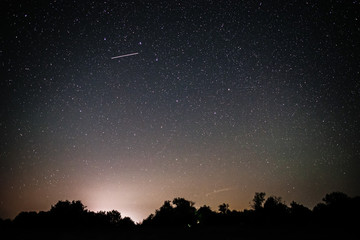 Background of bright starry night sky with lights upon on it and silhouette of trees