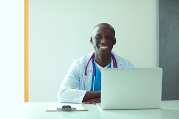 Portrait of young male doctor wearing headset while using computer at desk in clinic. Doctor.