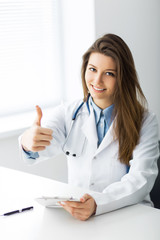 Smiling doctor showing thumb up while sitting in office