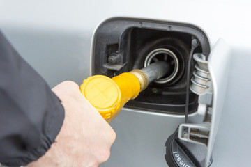 A man holding a yellow filling nozzle (gun) and is filling gas to a car tank. Valenciennes, France. 19 March 2017. 