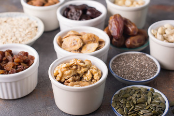 Ingredients for homemade granola, oats, different nuts and raisins, dates, seed on the grey stone background, selective focus
