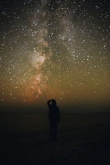 Silhouette of a lonely man standing on a sea beach and watching on the starry sky with Milky Way