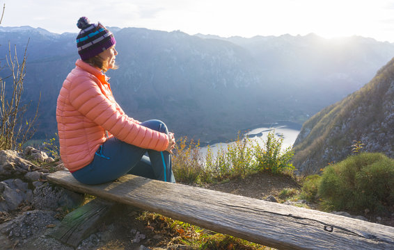 Young woman sitting on the branch on the viewpoint, relaxing after hiking and watching the Bohinj Lake, Slovenia
