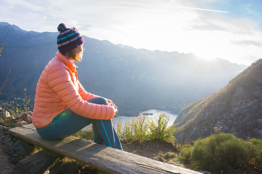 Young woman sitting on the branch on the viewpoint, relaxing after hiking and watching the Bohinj Lake, Slovenia