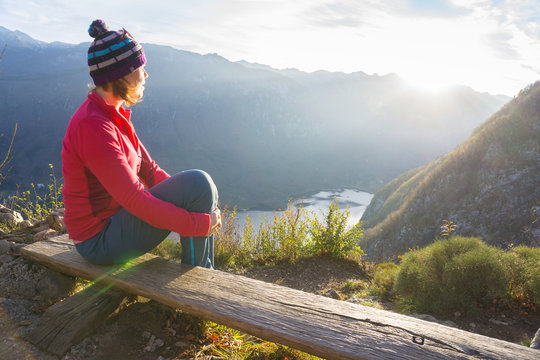 Young woman sitting on the branch on the viewpoint, relaxing after hiking and watching the Bohinj Lake, Slovenia