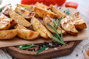 Board with delicious baked potatoes with rosemary on table