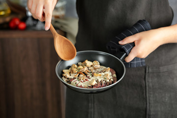 Woman holding frying pan with steak Diane and mushrooms, closeup