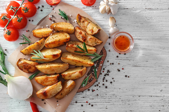 Board with delicious baked potatoes with rosemary on table