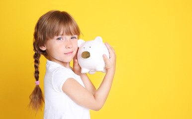 Cute little girl with piggy bank on color background