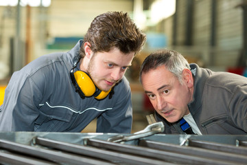 apprentice and teacher working with metal bars in a factory