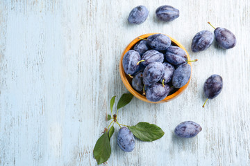 Bowl with ripe plums on wooden background
