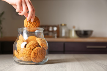 Woman taking oatmeal cookie from glass jar