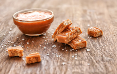 Candies and bowl with caramel topping on wooden table