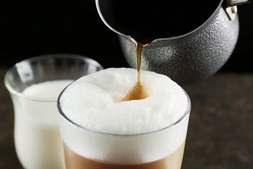 Adding coffee to latte macchiato on black background
