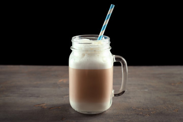 Mason jar with latte macchiato on table against black background