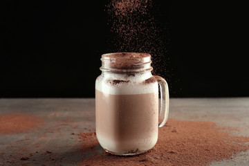 Pouring cinnamon powder into mason jar with latte macchiato on black background