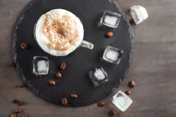 Glass with caramel macchiato and ice cubes on slate plate
