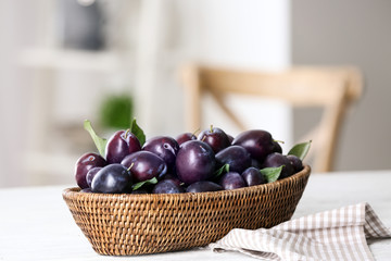 Fresh plums in wicker basket on table