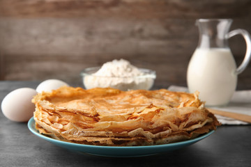 Plate with stack of delicious thin pancakes on table