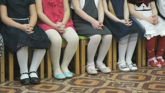 Unknown little children preschoolers in casual clothes sit on stools and posing for photographer in kindergarten in the classroom
