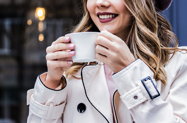 Enjoying good day. Cropped image of beautiful blonde woman keeping cup of coffee in hands and...