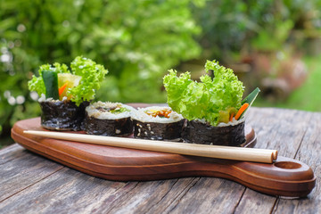 Kimbap  and chopstick on wooden cutting board with blurred banckground. Kimbap is a Korean dish made from steamed white rice  and various other ingredients.