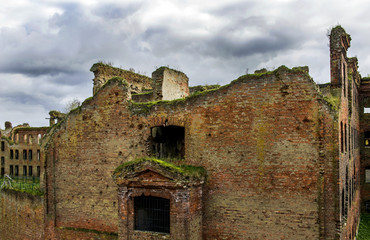 A war-torn building of red brick, broken windows, gloomy sky. The concept of the consequences of war and destruction. Northern Europe. Ruins of an old prison.