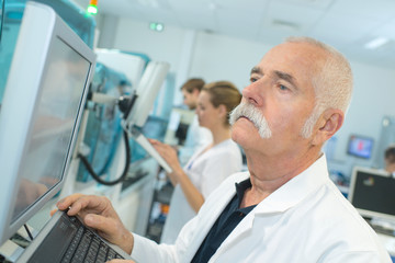 senior male pharmacist in a white lab checking results