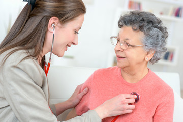 female caregiver examining senior woman with stethoscope