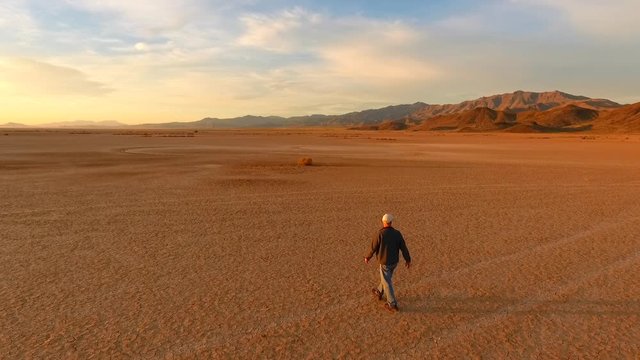 A man walking on a barren dry lake in the desert as if lost