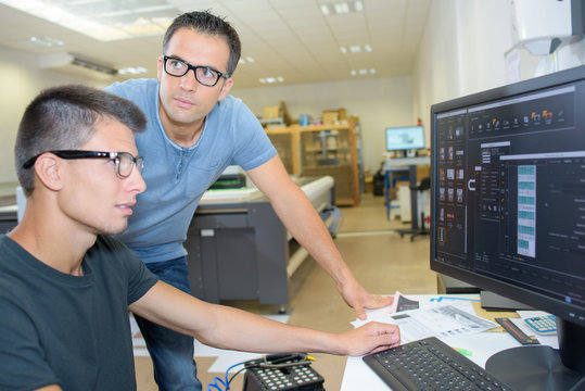 Two men wearing glasses working on a computer