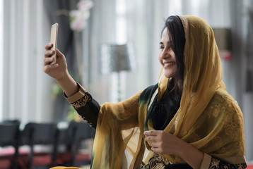Muslim woman in yellow dress taking selfie. - obrazy, fototapety, plakaty