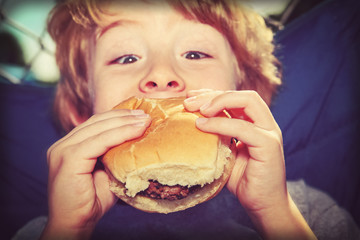 young boy eating a hamburger outdoors, vintage instagram effect.