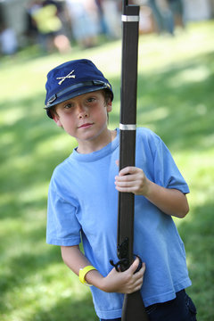 Boy at a Civil War re-enactment wearing a union soldier hat and holding a toy gun.
