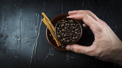 A man's hand holds a cup of coffee beans with cinnamon