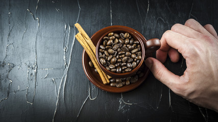 A man's hand holds a cup of coffee beans with cinnamon