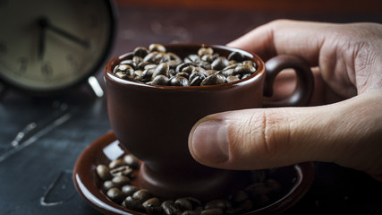 A man's hand holds a cup of coffee beans with alarm clock