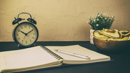 Plate with muffins notebook with pen and alarm clock concept of breakfast while working