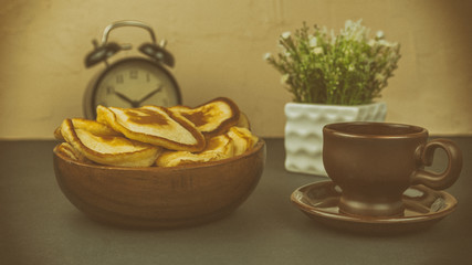 A cup of coffee and a plate of fritters and an alarm clock and a flower in a pot of the morning breakfast concept