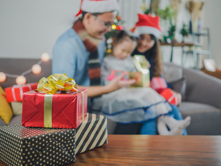 Focus gift box and blurred background asian young family on Christmas exchanging presents and...