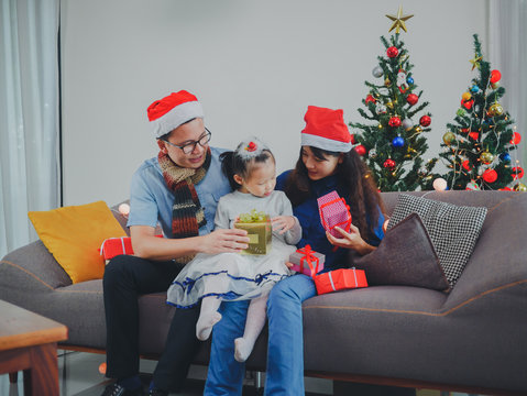 Asian Young Family On Christmas Exchanging Presents And Enjoying Their Time Together. Focus On The Little Girl.