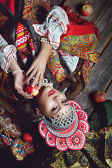The girl in the folk style and bright make-up holding an Apple on dark wooden background top view