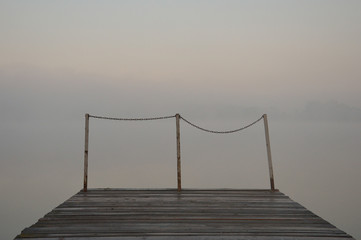Asymmetry concept - asymmetric railings at the end of a lake pier with a morning mist background