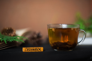 The inscription is December. Winter photography with books, a cup of tea, cones, branches of a Christmas tree. On a black wooden background lie books and a cup of tea. A card with a place for your tex