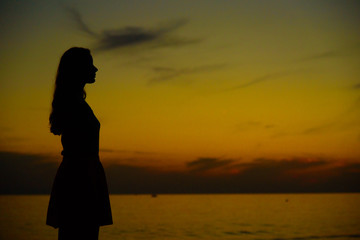 Lonely girl watching sunset near the sea or ocean