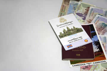 The concept of travel in Cambodia. The pile of document, Arrival and Cambodia departure card on the postcard on the Thai passport on the Cambodian banknotes with white background.