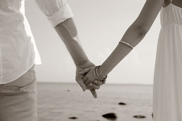 Detail of young couple holding hands on beach background , sepia